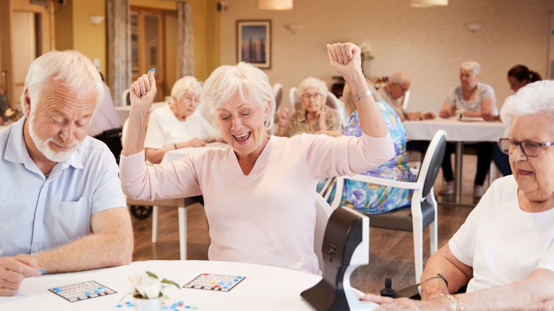 Tre glada seniorer vid ett bord spelar bingo.