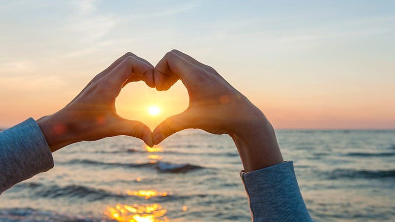 Gör en hjärtagest med händer och solnedgång i bakgrunden.